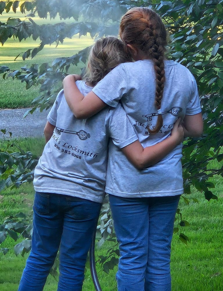 Two daughters hugging outdoors while wearing matching locksmith work shirts
