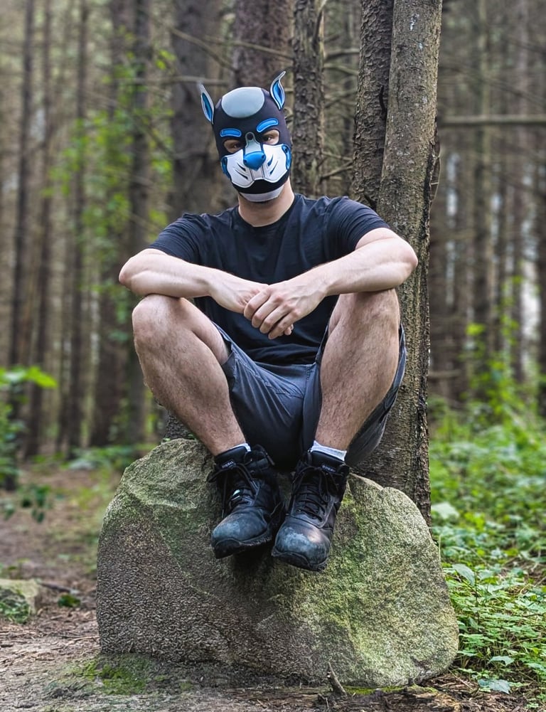 A man sitting in the woods wearing a pup mask.