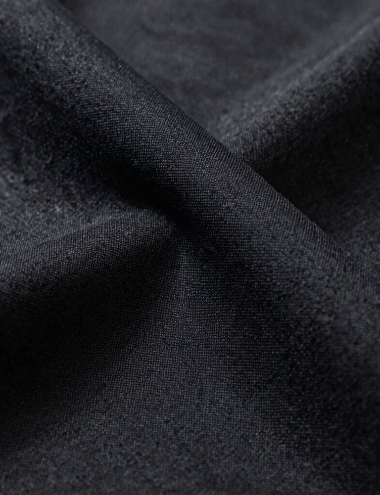 A close-up shot of a luxury fabric texture in deep charcoal and black, dramatic side lighting highlighting the quality and detail, North American studio style.