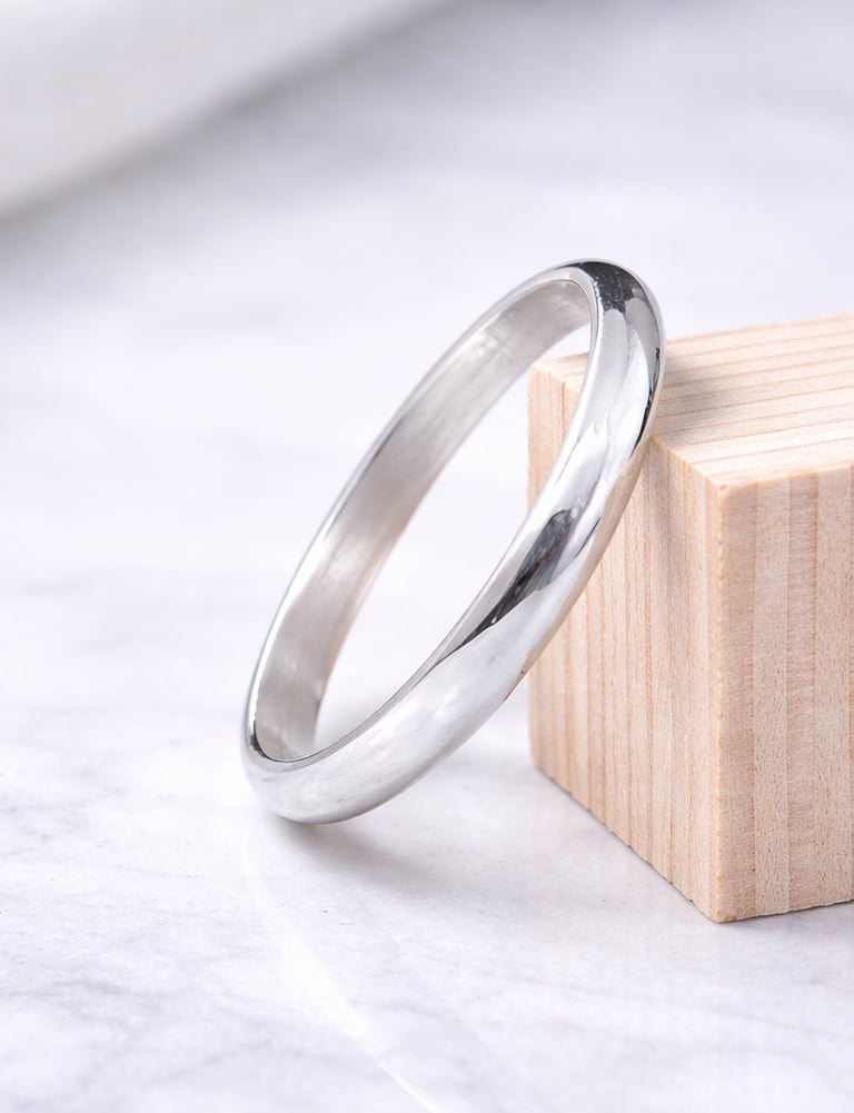 Minimalist polished 999 fine silver wedding band resting on a wooden block over a marble surface.