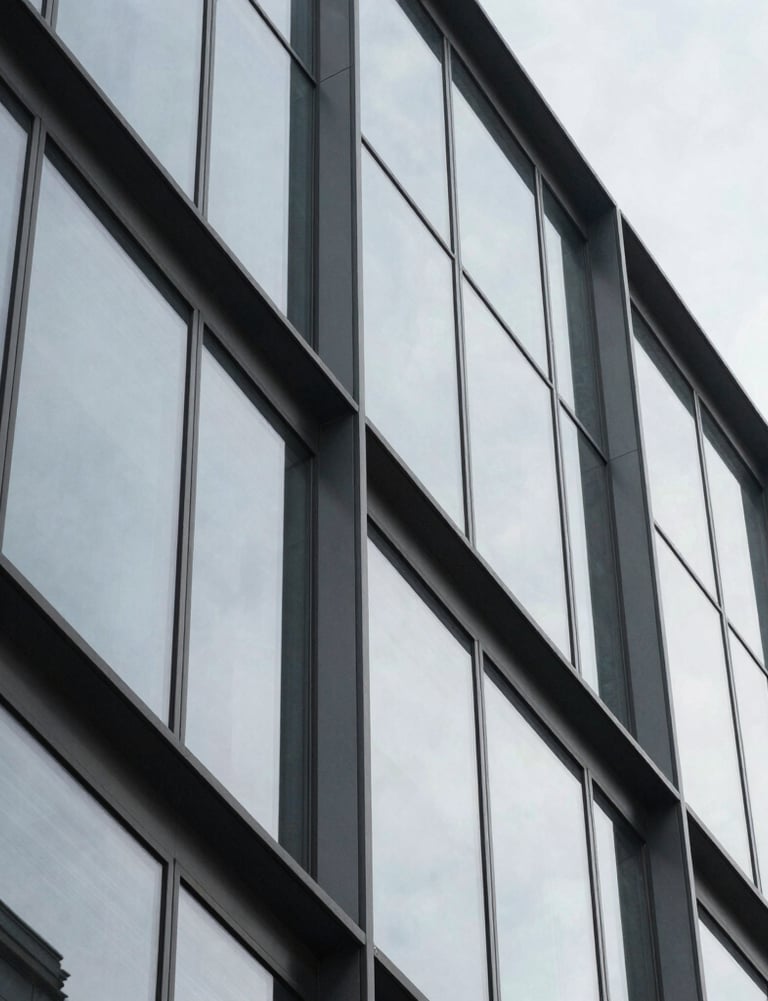 Abstract architectural detail of a modern glass building featuring sharp geometric shapes and reflections in light gray tones. International / Professional.