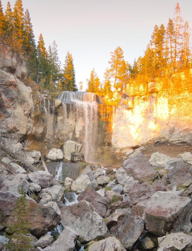 Paulina Falls waterfall flowing over rocky cliffs in Central Oregon at sunset.
