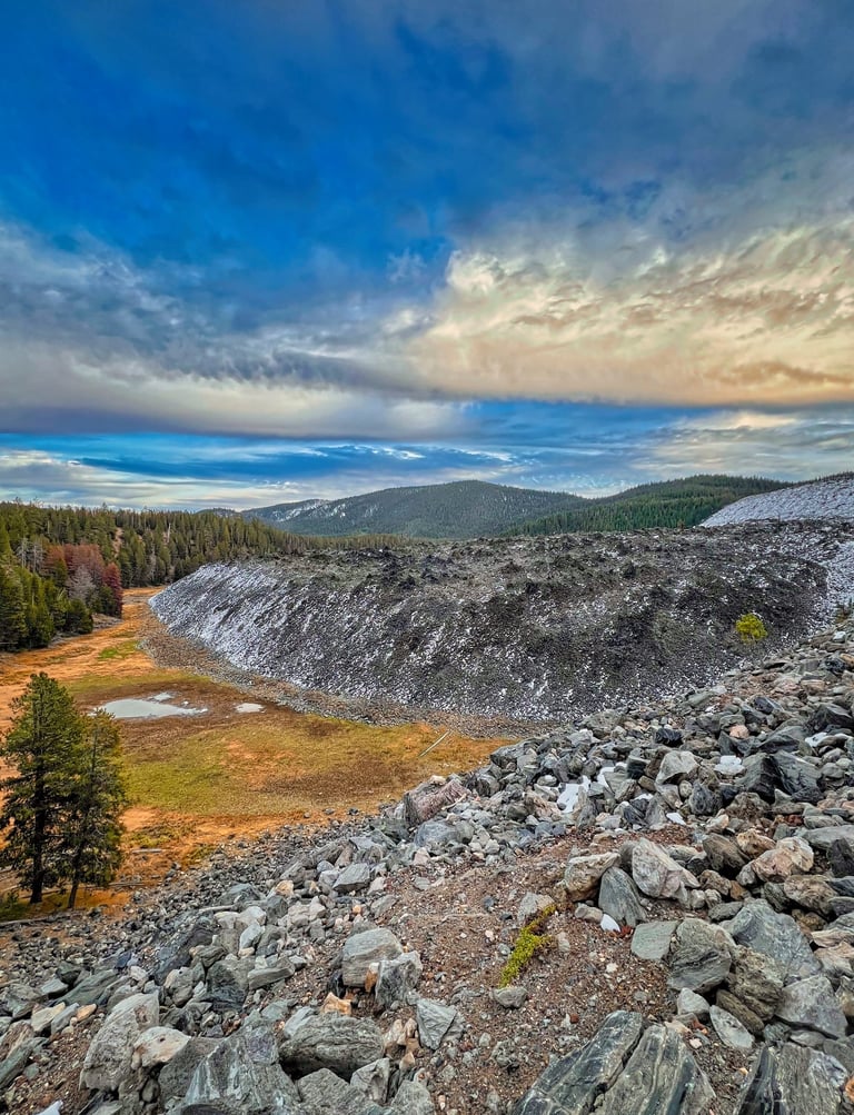 Scenic mountain landscape featuring a rocky talus slope and pine forest under a dramatic cloudy sky.