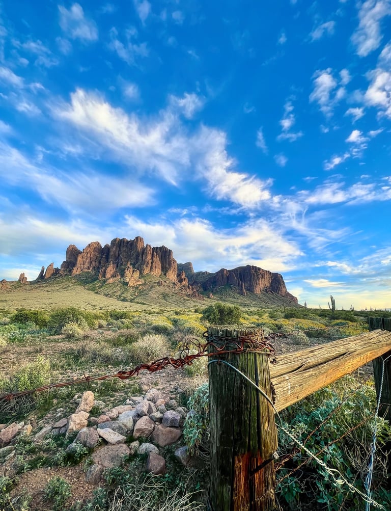 Rustic wooden fence overlooking the Superstition Mountains in the Arizona desert under a blue sky.