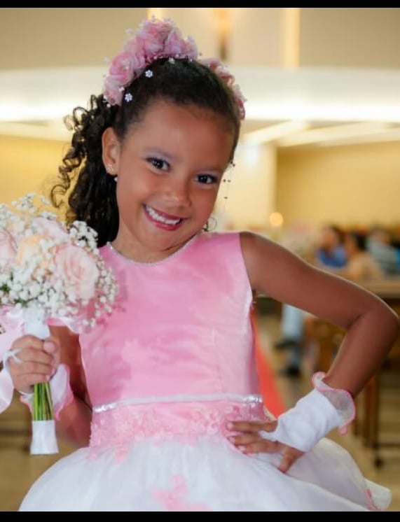 menina de 9 anos com vestido rosa e branco e um buque de fleres nas maos.