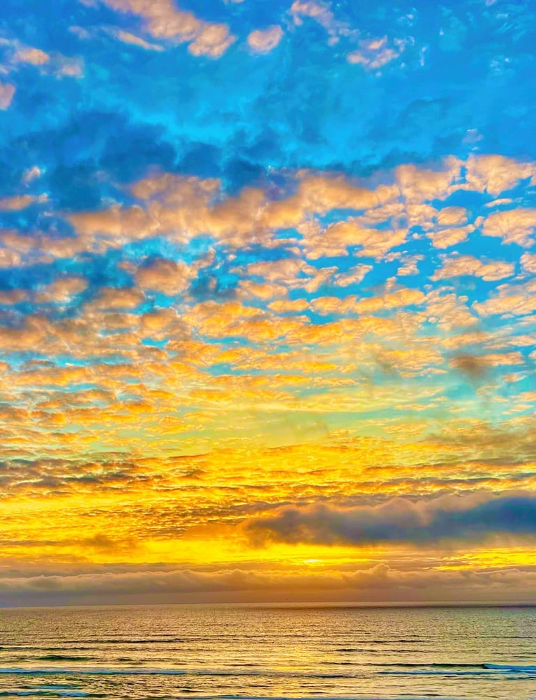 Vibrant ocean sunset with golden light reflecting on waves under a blue sky with fluffy altocumulus clouds.