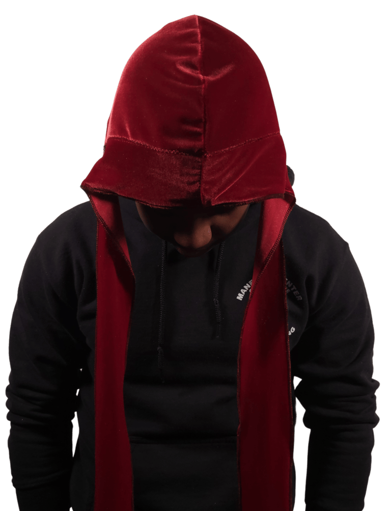 A man wearing a luxurious red velvet Taji over a black hoodie against a dark background.