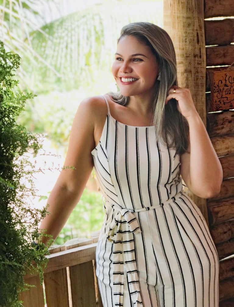 Priscila, Pri Cílios extensionista de cílios, sorrindo em fazenda com vestido branco.