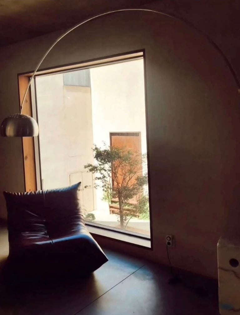 Modern living room featuring a leather Togo chair, large window with a view, and an arched floor lamp.