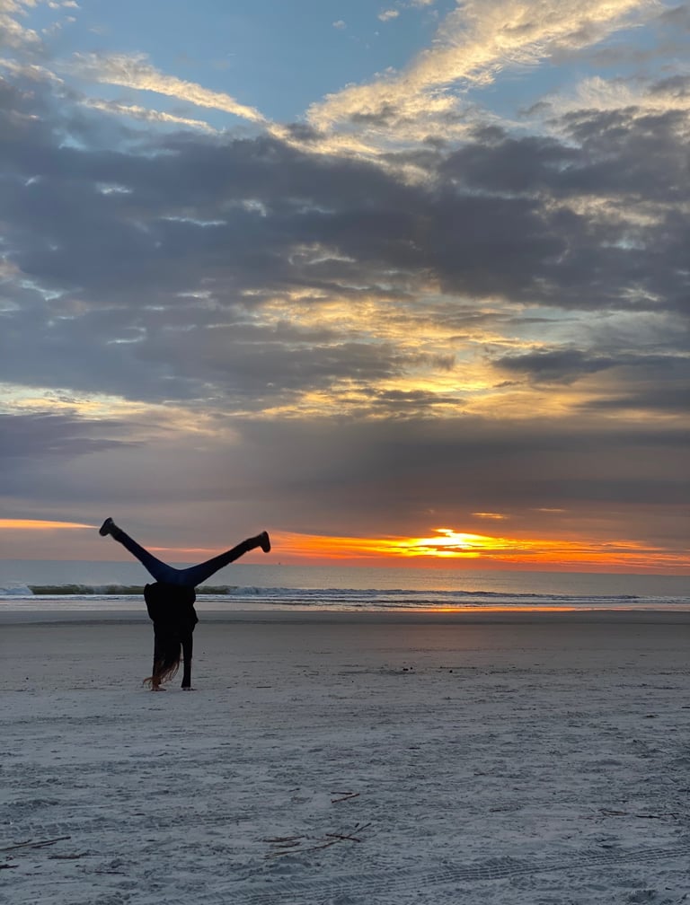 A woman doing a cartwheel on the beach silhouetted by the sunrise