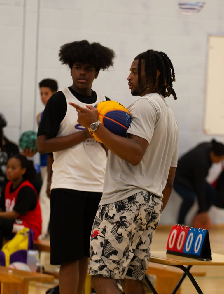 Basketball coach holding a ball and instructing a young player during an indoor sports training session.