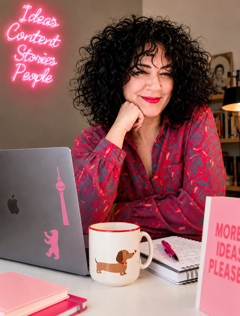 Content creator with curly hair working at a desk with a laptop and neon sign.