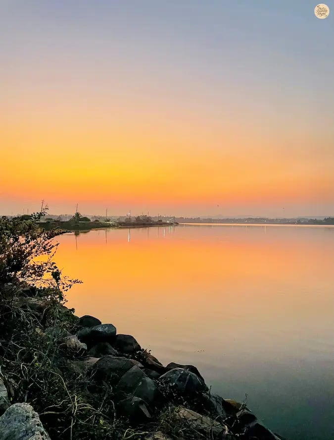 Sunset over Kamalapur Lake in Hampi with pink-hued sky reflecting on the water.