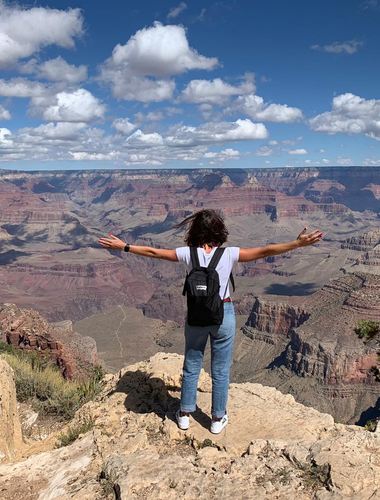 A female hiker stands with arms wide open overlooking the vast Grand Canyon National Park landscape.