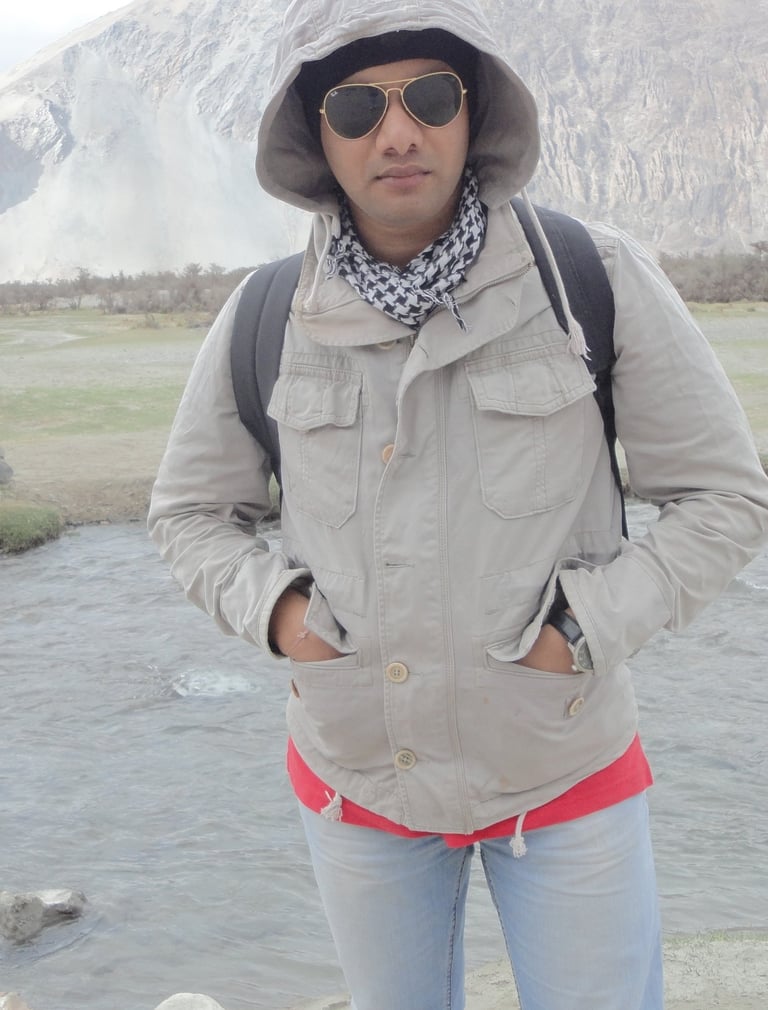a man in a hat and sunglasses standing in front of a mountain, raheel ahmed