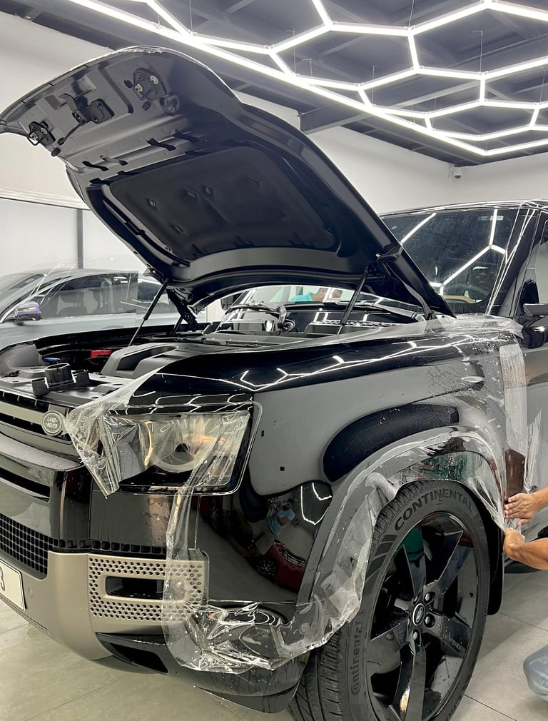 Professional paint protection film application on a black Land Rover Defender in a detailing studio.