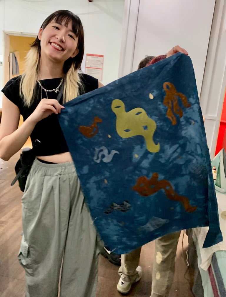 A person with blonde and black hair and light skin holds a banner smiling.
