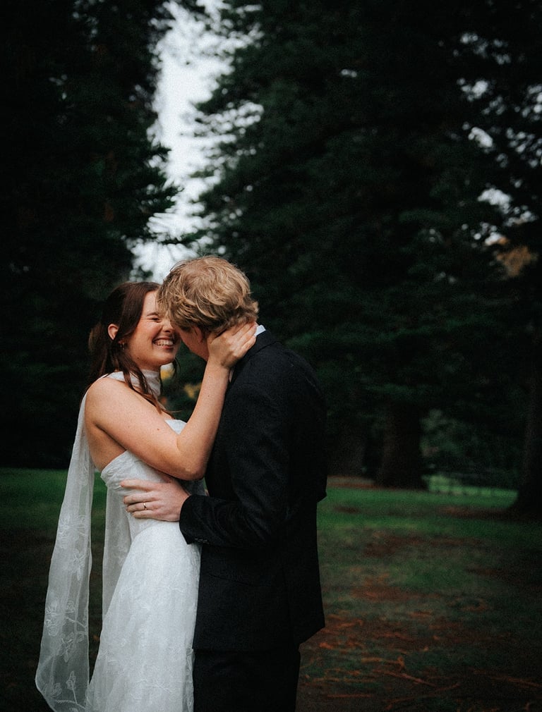 Smiling bride and groom embrace during a moody outdoor wedding photoshoot in a forest.