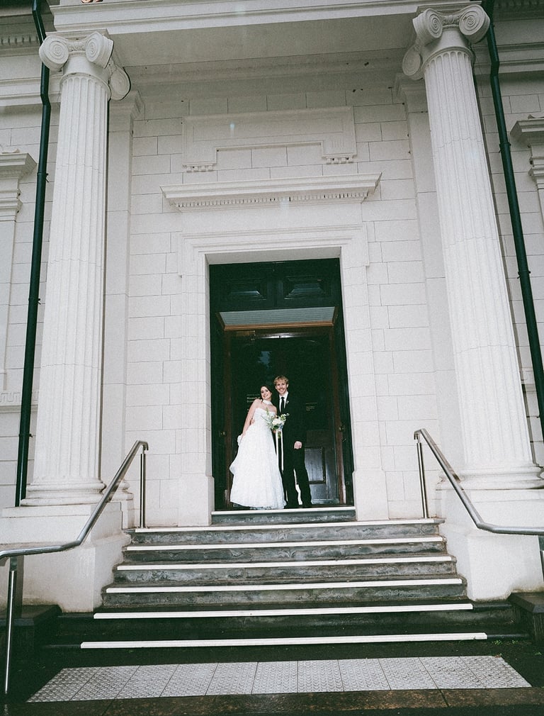 A bride and groom posing at the entrance of a historic building with large white columns.