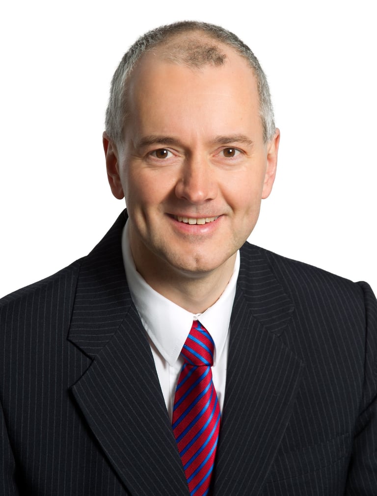 Jörg Grube Portrait Foto mit weißem Hemd, Jackett, Krawatte in den Farben rot und blau gestreift