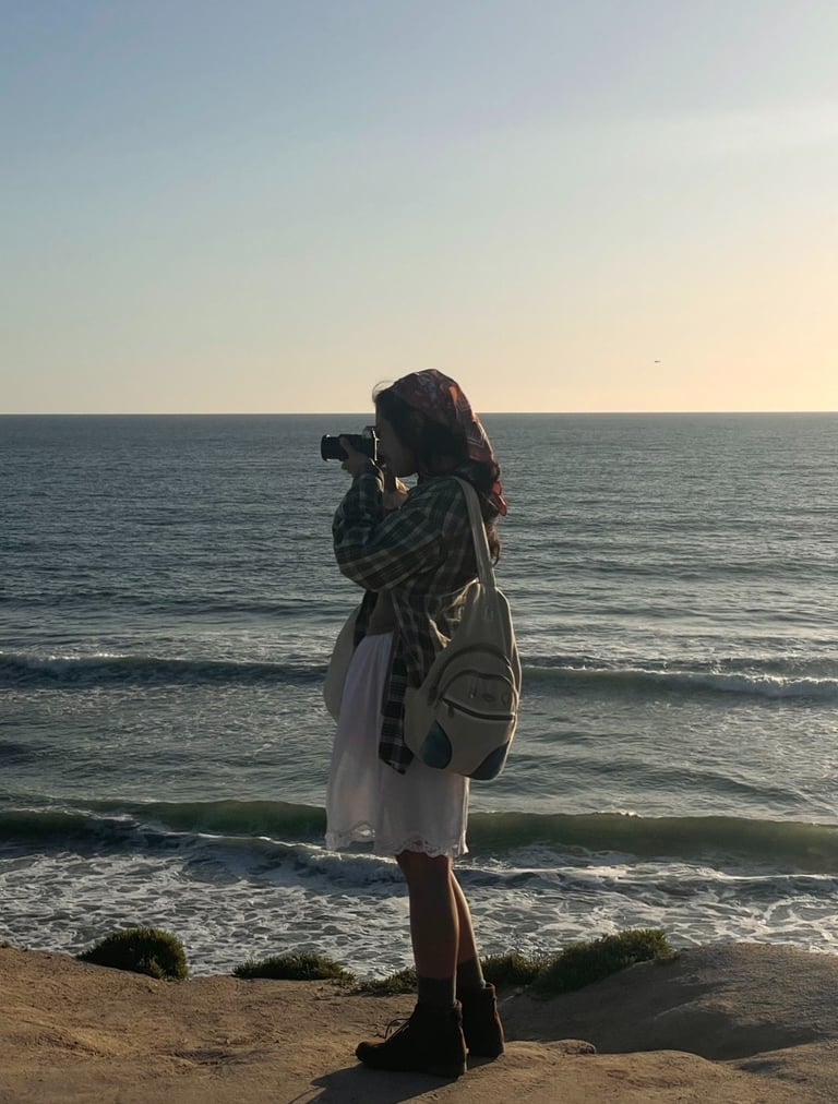 Vibey full body candid shot of me holding camera up to my face, standing on cliffs over ocean.Earthy