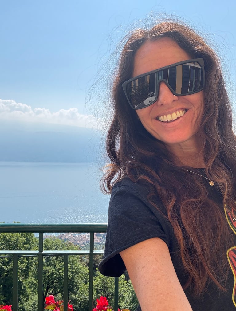 Michael Alexa Pitts smiling in the sunny, blue sky day on a mountainside with Lake Garda, Italy down below in the background