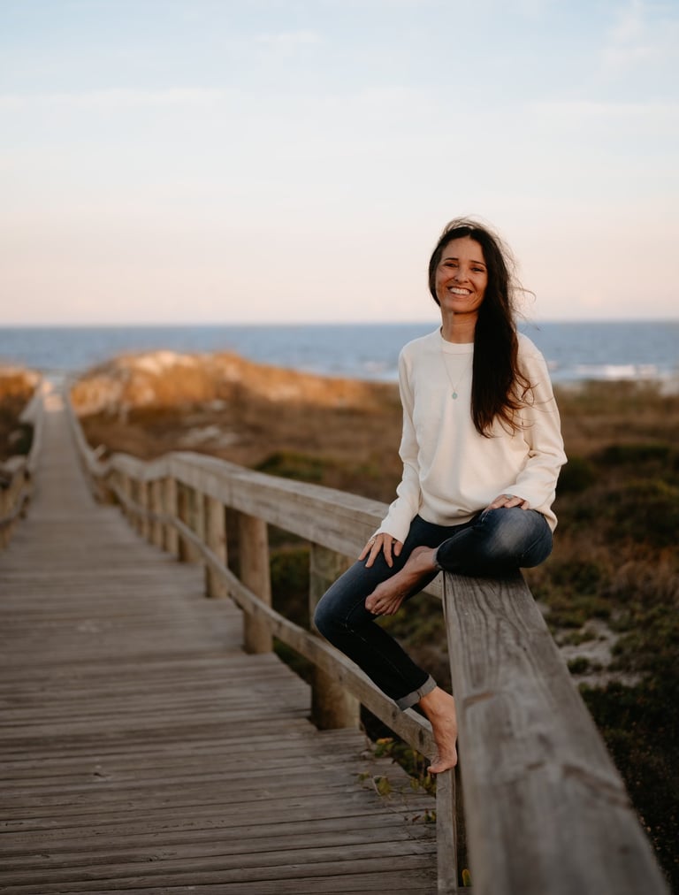 Michael Alexa Pitts smiling & sitting on the railing of a boardwalk path over the sand dunes & down to the beach near sunset