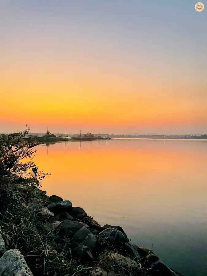 Sunset over Kamalapur Lake in Hampi with pink-hued sky reflecting on the water.