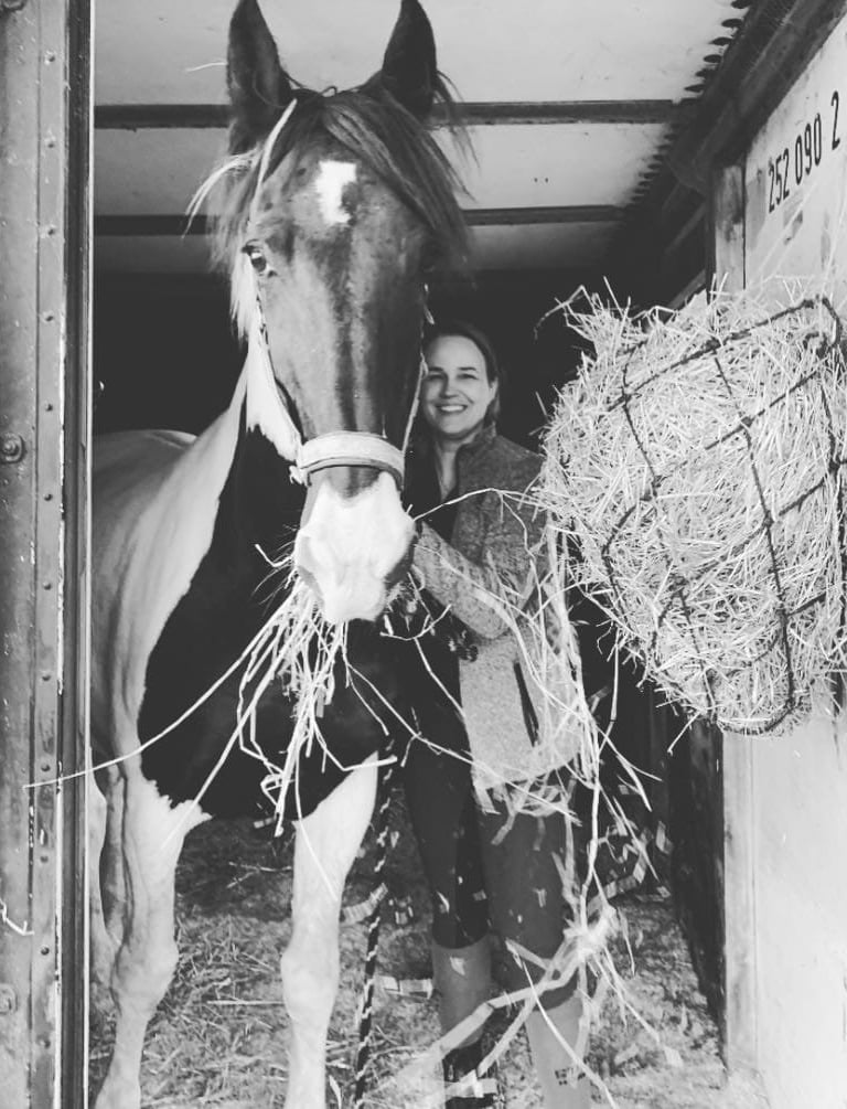 Jennifer en haar paard Fayah staan samen in de deuropening van de stal