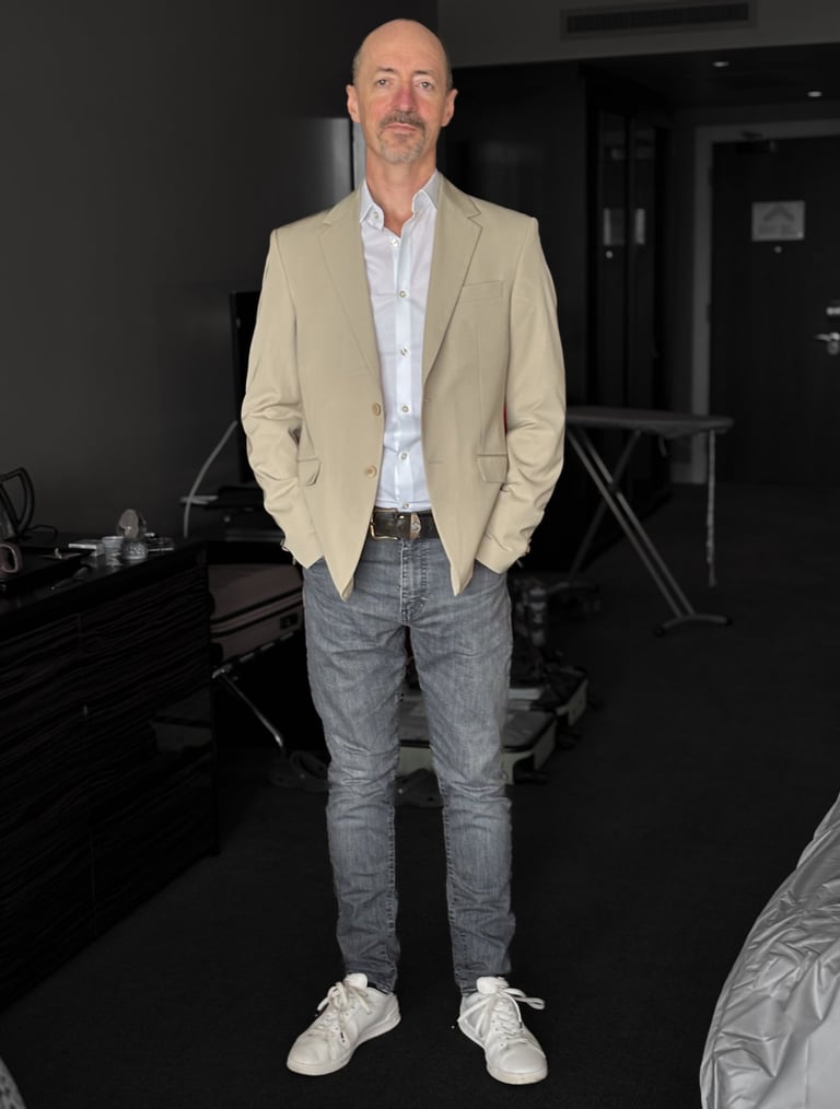 Portrait photo of Mark Murfitt wearing a cream colored jacked, white shirt, black jeans