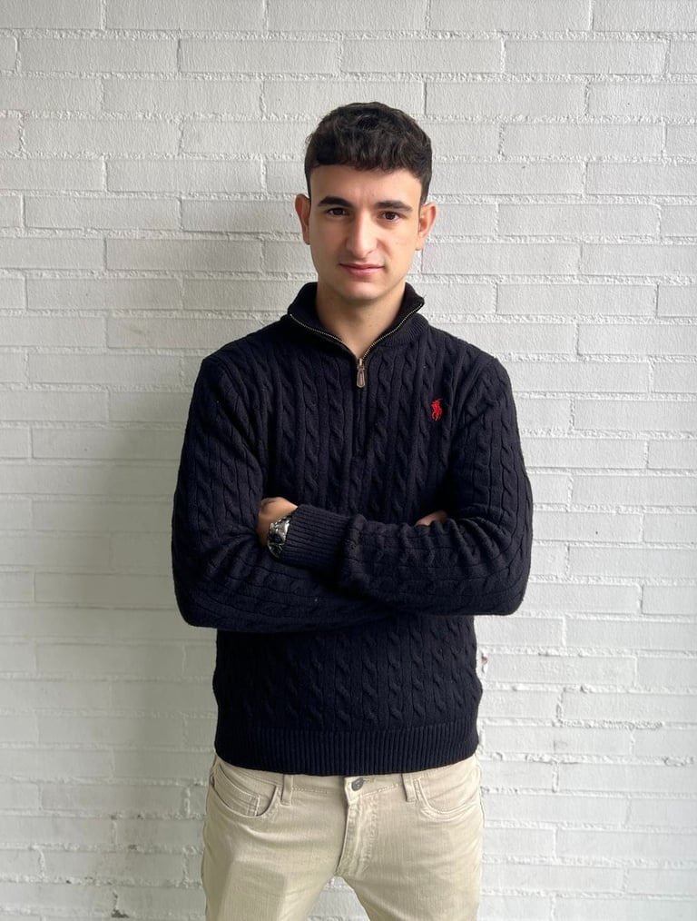 a man in a sweater and jeans standing in front of a white brick wall
