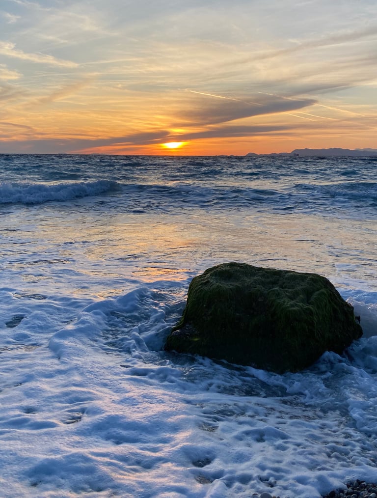 Golden sunset over ocean waves with a moss-covered rock in the white sea foam.