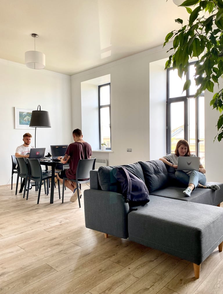 Three people working on laptops in a bright, modern open-plan home office with a grey sofa.
