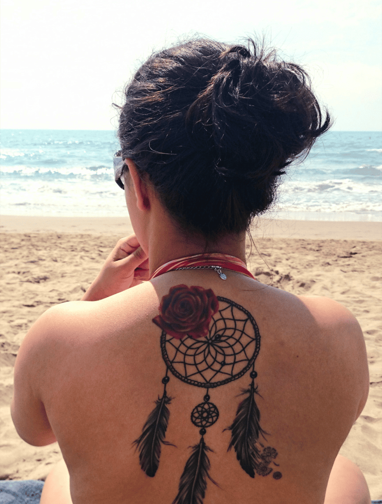 Femme de dos sur la plage, tatouage de rose et capteur de rêves, symbole de mémoire et lignée spirit