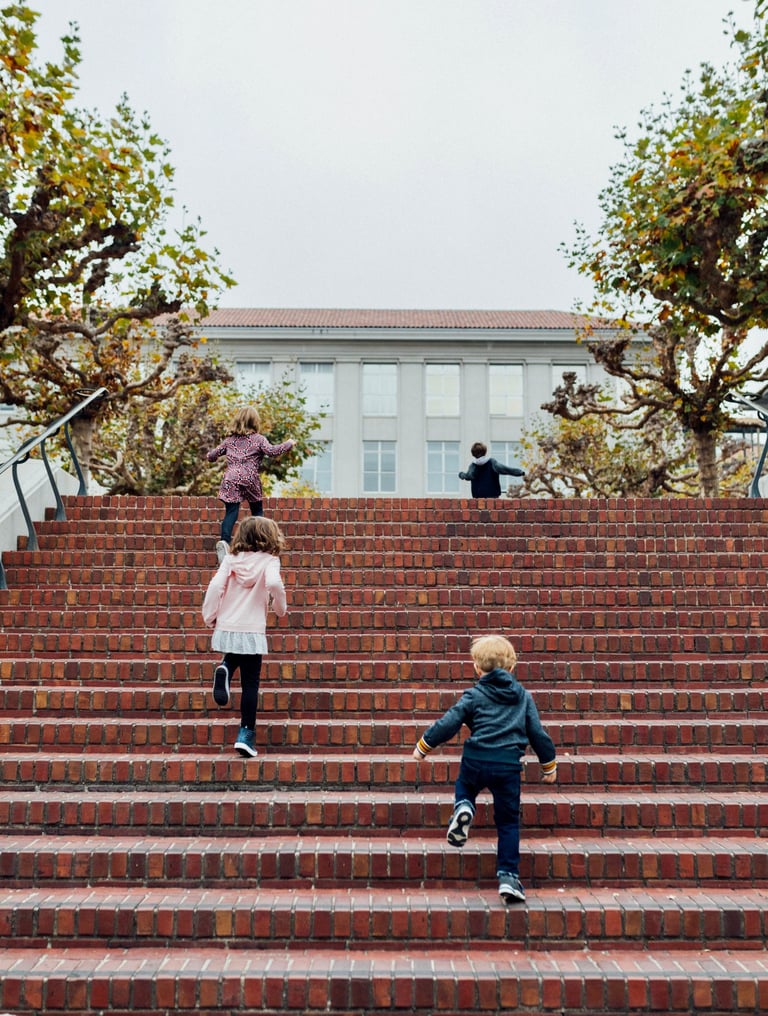 Four small children running up stairs towards a building