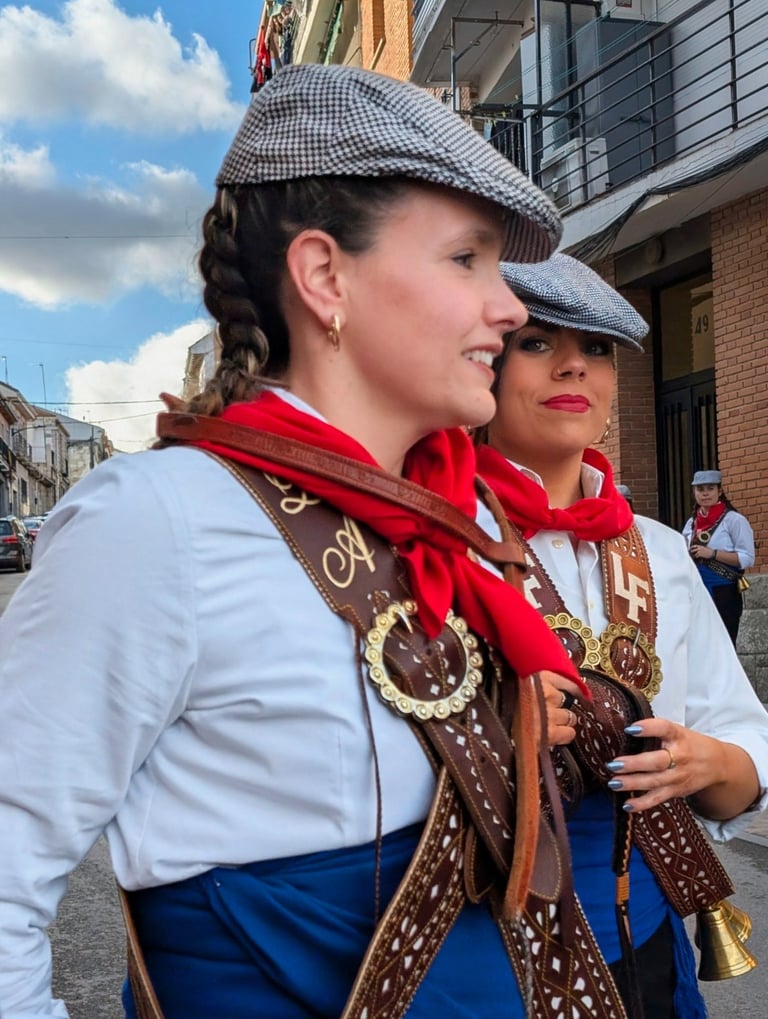 Close-up of two women in traditional Spanish festival attire with papusas, red scarves, and leather harnesses.