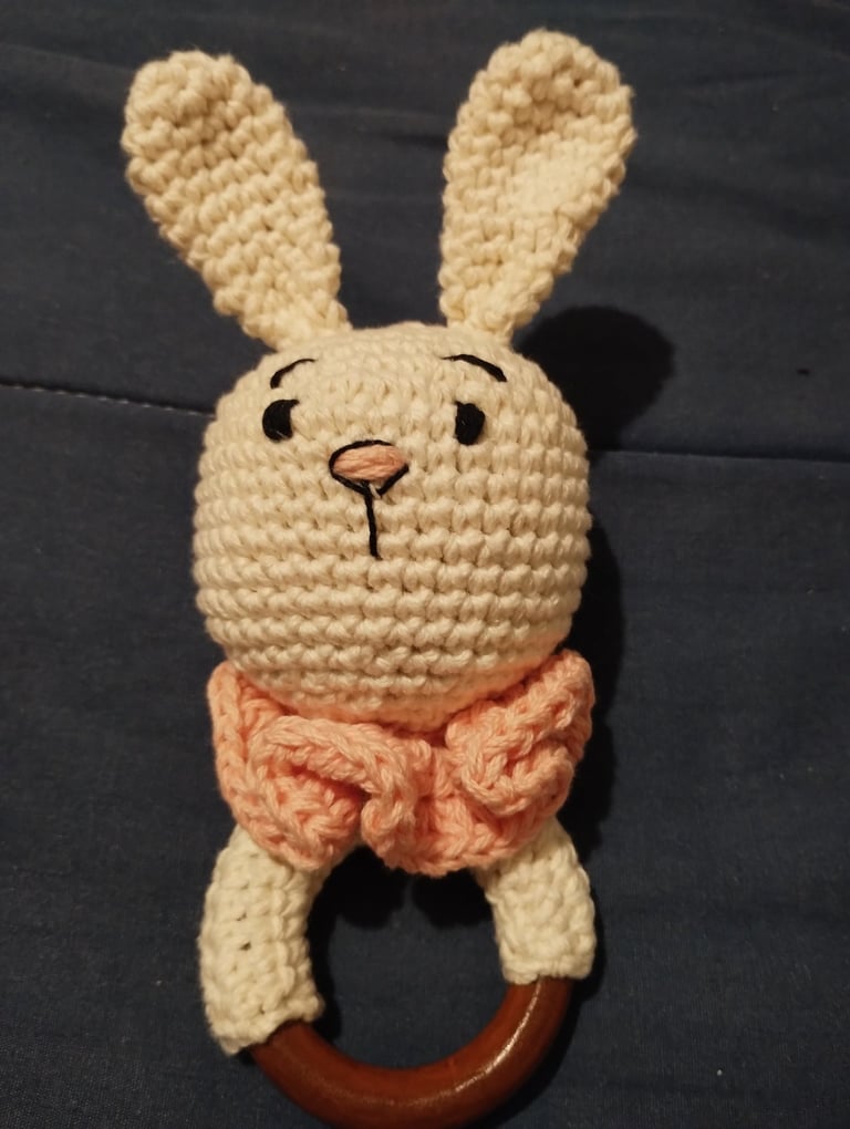 Sonajero de bebé de ganchillo hecho a mano en color crema con forma de conejito y asa de aro madera.