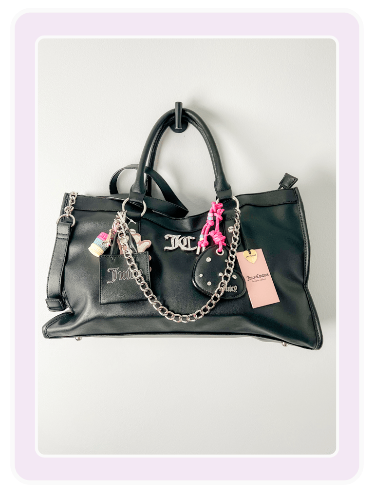 Black Juicy Couture tote bag with silver chain, logo hardware, and colorful charms hanging on a hook.