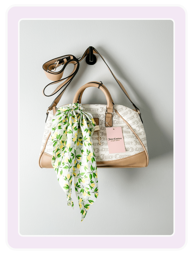 Cream Juicy Couture satchel handbag with tan trim and a lemon print scarf hanging on a wall hook.