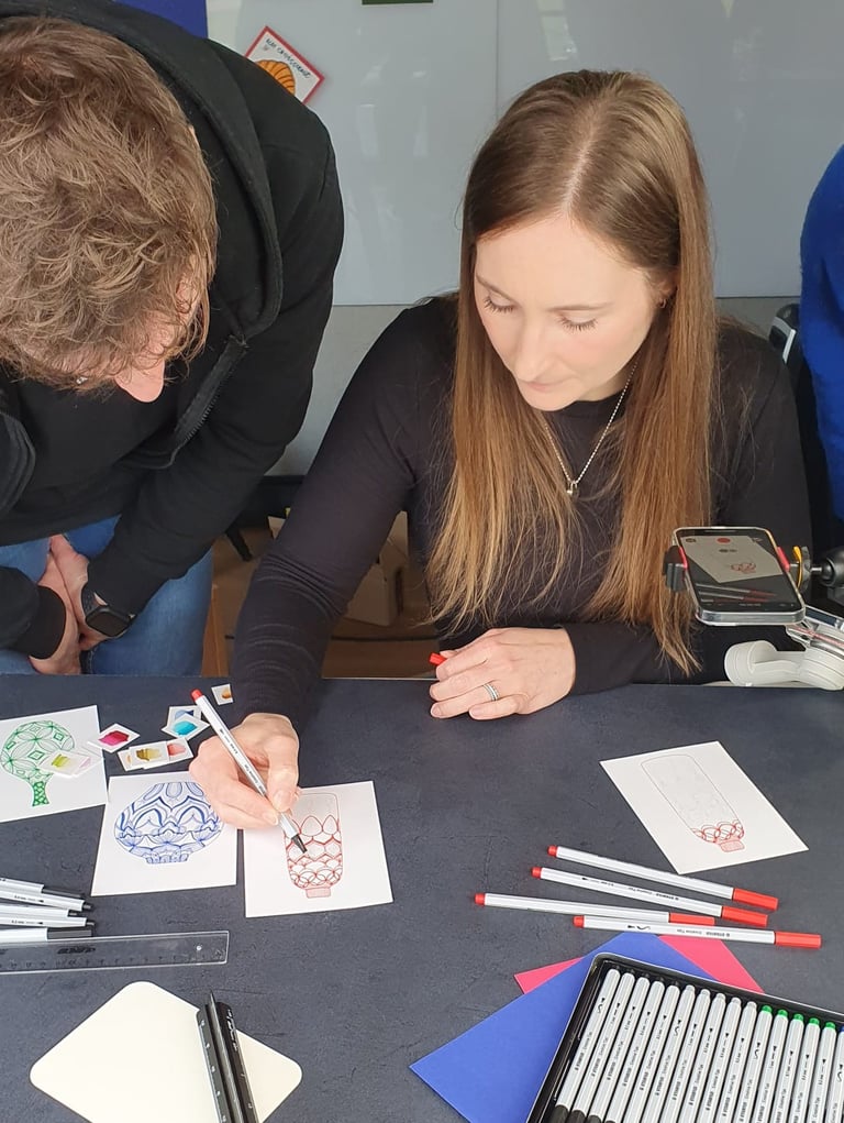 A woman uses a fine-liner pen to illustrate a creative design on paper during an art workshop.