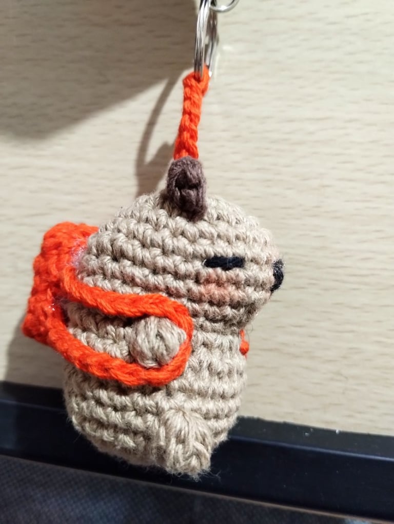 Llavero amigurumi de capibara marrón hecho a mano en ganchillo, con mochila naranja.