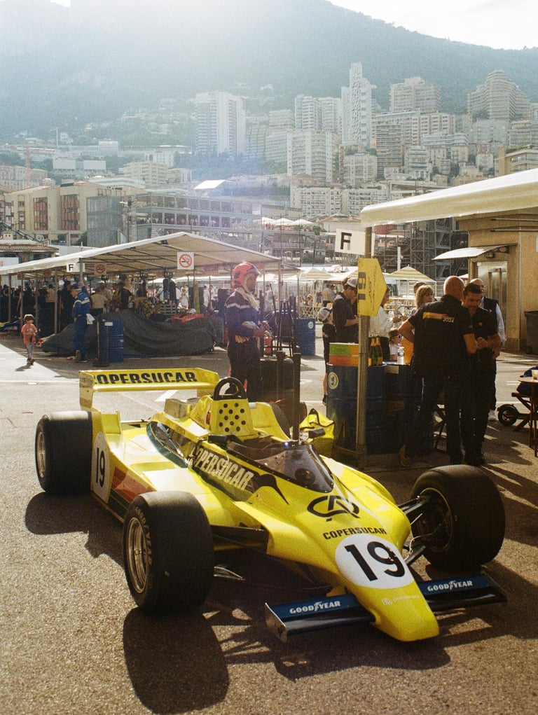a yellow 80's Formula 1 car with a number of people standing around it