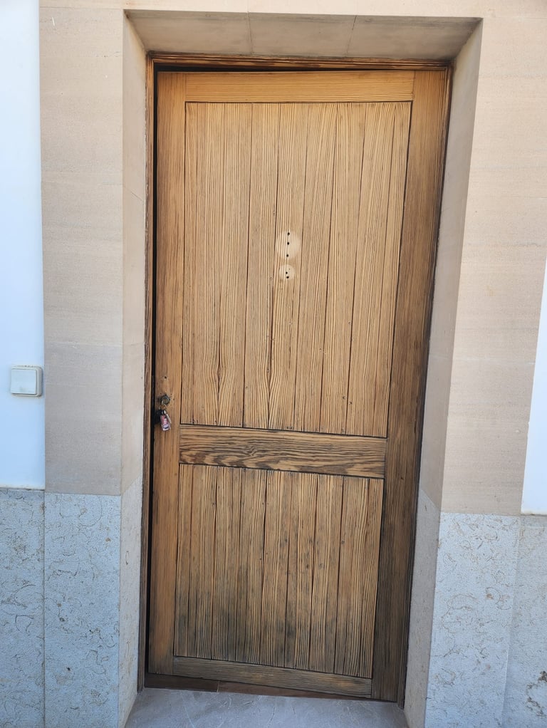 Rustic vertical grain wooden exterior door set in a stone door frame with a small key in the lock.