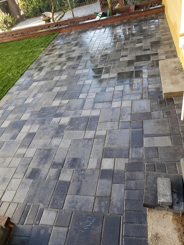 Backyard landscaping with modern grey interlocking pavers and vibrant artificial grass lawn creating