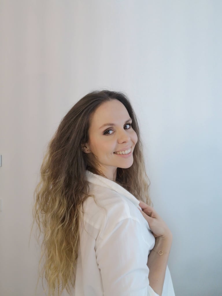 Smiling woman with long wavy brown hair wearing a white button-down shirt against a neutral background.