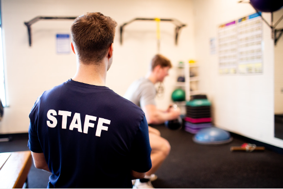 coach with staff shirt training a man in a gym