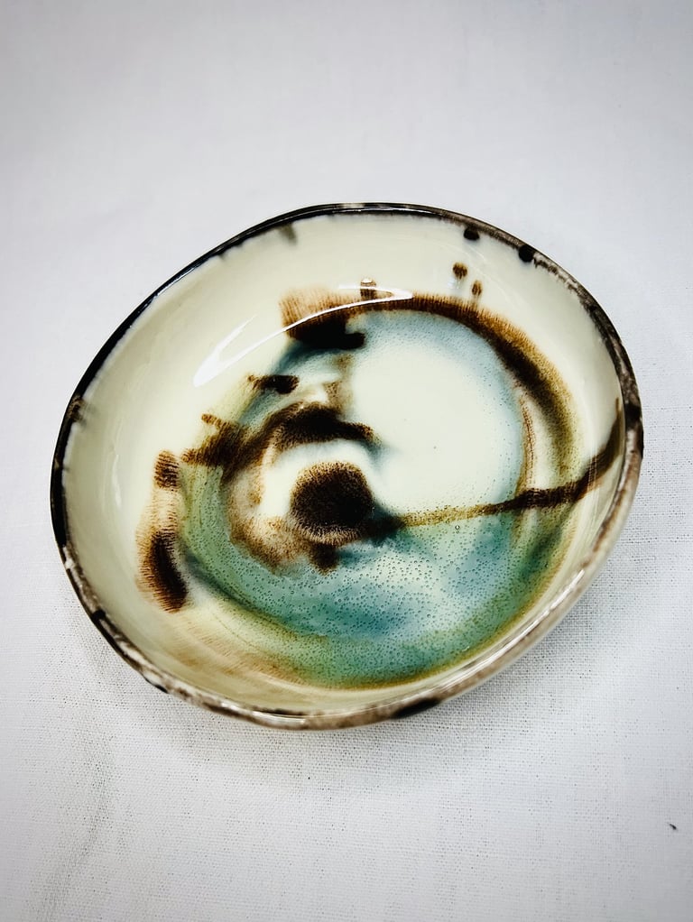 A glazed plate with black lid and abstract brown and green spots and shades