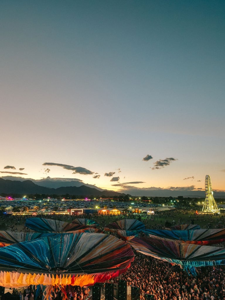 Crowds at an outdoor music festival at sunset with a Ferris wheel and colorful shade structures.
