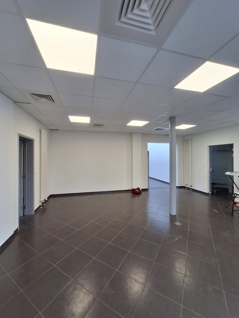 Une photo avant transformation de l'ancien showroom avec des murs blanc et un sol gris 