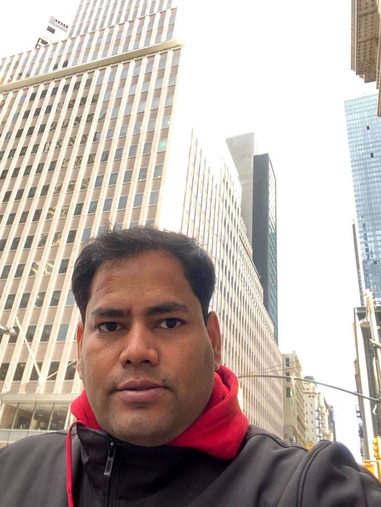 A man in a red hoodie and black jacket taking a selfie among tall skyscrapers in New York City.